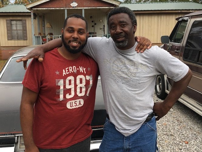 Two Black men with their arms around each other, smiling at the camera